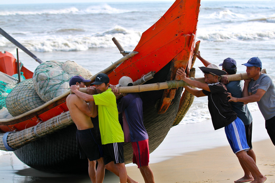 Ngư dân khiêng thuyền xuống biển để ra khơi. (Ảnh: Hồ Cầu - TTXVN)