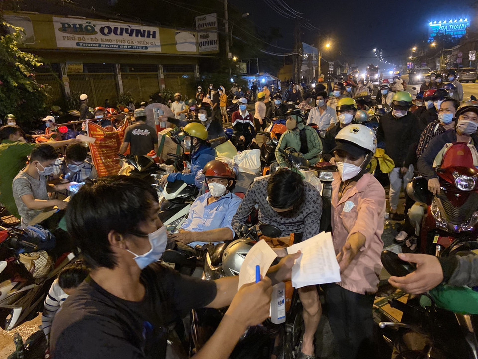 Lực lượng chức năng hướng dẫn người dân ghi phiếu thông tin chốt kiểm soát khu vực cửa ngõ trên Quốc lộ 1A, giáp ranh giữa Thành phố Hồ Chí Minh và tỉnh Long An trong đêm 30/9. (Ảnh: Mạnh Linh/TTXVN)