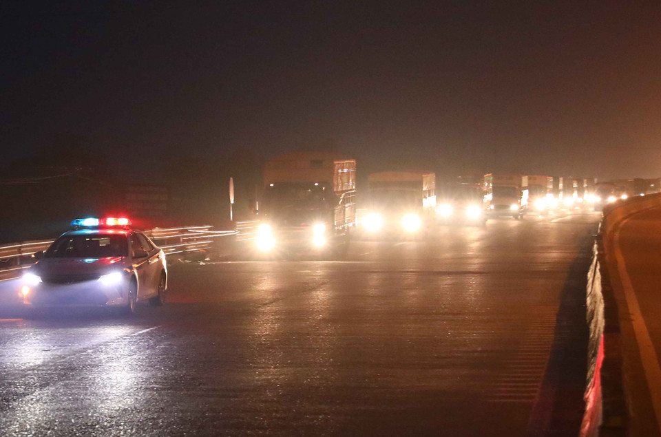 Đúng 5h10, xe cảnh sát giao thông tỉnh Hà Nam bắt đầu dẫn hàng chục xe tải biển kiểm soát tỉnh Ninh Bình chở theo khoảng 1.000 người và xe máy phía sau thùng xe về đến chốt kiểm soát dịch số 1, QL 1A, huyện Phú Xuyên, Hà Nội. (Ảnh: Phạm Kiên/TTXVN)