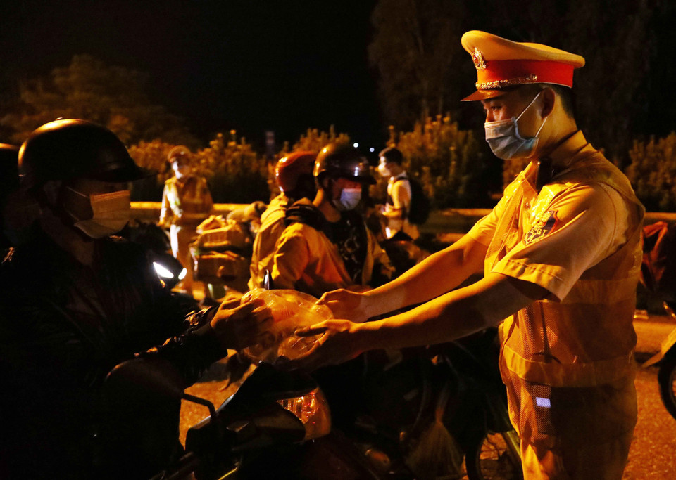 Cán bộ cảnh sát giao thông hỗ trợ đồ ăn, nước uống cho người dân đi từ vùng dịch phía Nam về quê qua địa bàn Hà Nội. (Ảnh: Phạm Kiên/TTXVN)