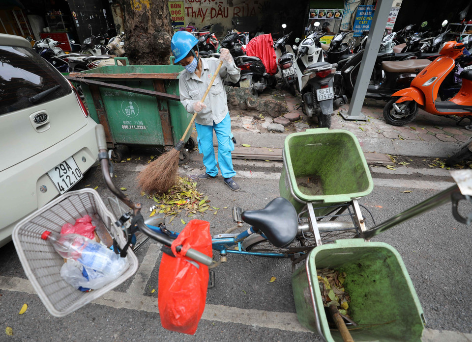 Với chiếc xe đạp và vật dụng quen thuộc (chổi, xẻng) người công nhân này đi sau các xe ôtô thu gom rác để làm sạch lần nữa nơi đặt các thùng rác trên phố. (Ảnh: Thanh Tùng/TTXVN)