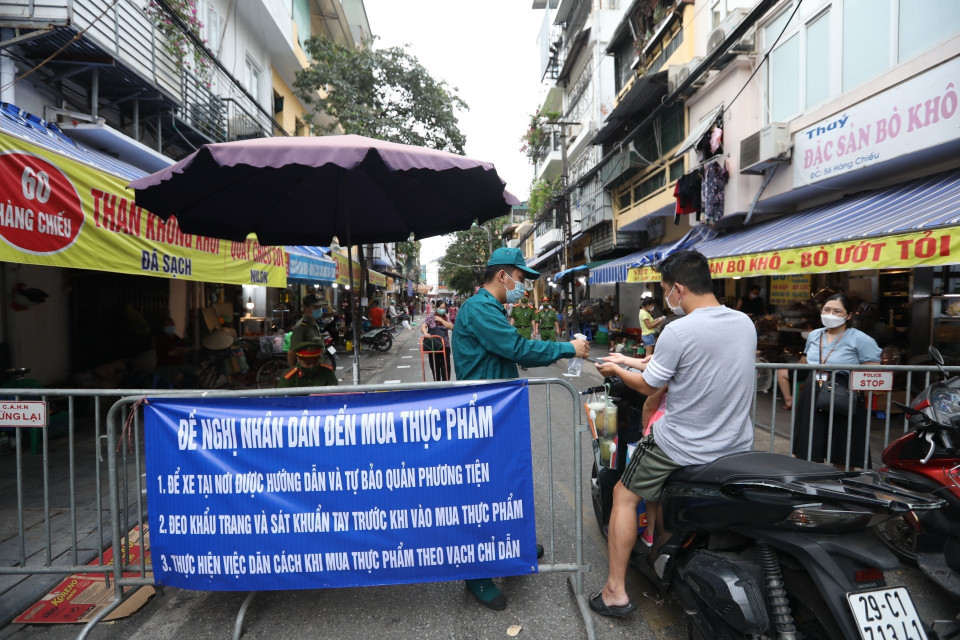 Lực lượng chức năng phường Đồng Xuân, quận Hoàn Kiếm kiểm soát, xịt sát khuẩn tay cho người vào chợ tại khu mua sắm hàng thiết yếu trên phố Nguyễn Thiện Thuật (ảnh chụp sáng 26/7). (Ảnh: Minh Quyết/TTXVN)