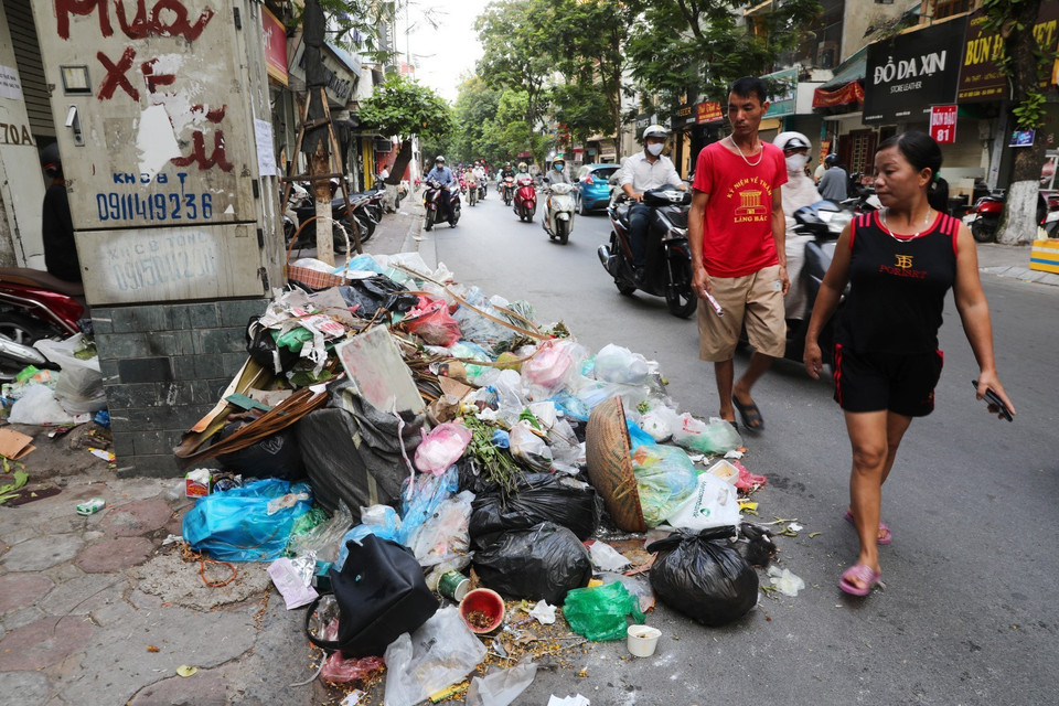 Cái nắng lên tới 40 độ C khiến cho những đống rác này bốc mùi hôi thối nồng nặng, khiến người qua đường chỉ biết "nhắm mắt nín thở" tại phố Đội Cấn (ảnh chụp ngày 16/7). (Ảnh: Thành Đạt/TTXVN)