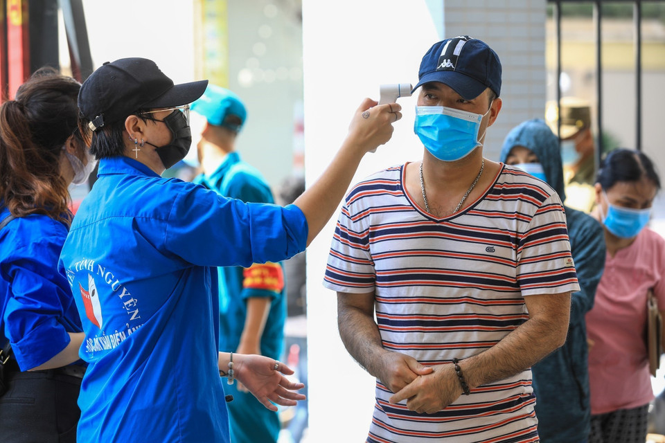 Sinh viên tình nguyện kiểm tra nhiệt độ cho người dân đến mua bánh tại Tiểu học Chu Văn An. (Ảnh: Thành Đạt/TTXVN)