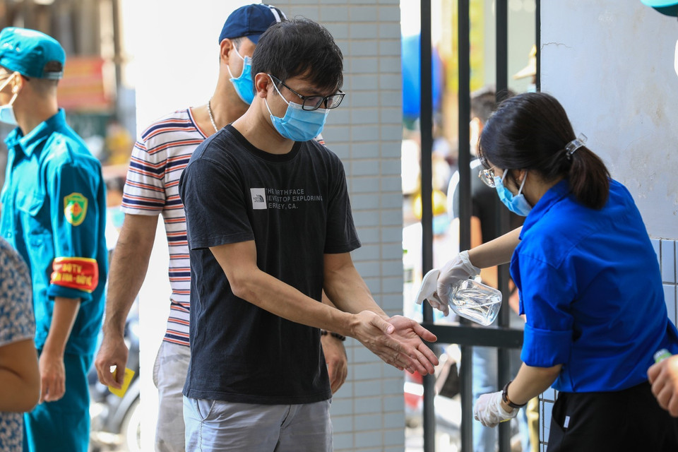 Sinh viên tình nguyện xịt khử khuẩn và kiểm tra nhiệt độ cho người dân đến mua bánh tại Tiểu học Chu Văn An. (Ảnh: Thành Đạt/TTXVN)