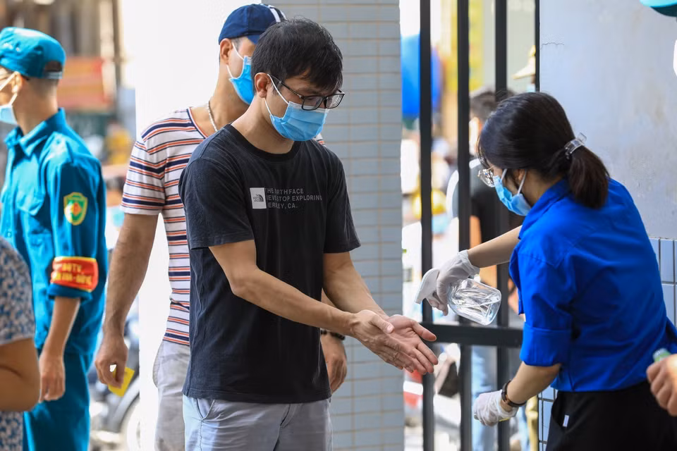 Sinh viên tình nguyện xịt khử khuẩn và kiểm tra nhiệt độ cho người dân đến mua bánh tại Tiểu học Chu Văn An. (Ảnh: Thành Đạt/TTXVN)