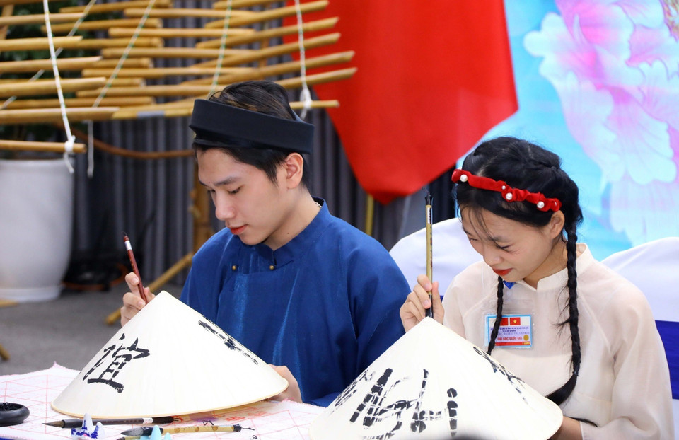 Sinh viên Đại học Quốc gia Hà Nội viết chữ trên nón lá truyền thống Việt Nam để gửi tặng hai Phu nhân. (Ảnh: Văn Điệp/TTXVN)