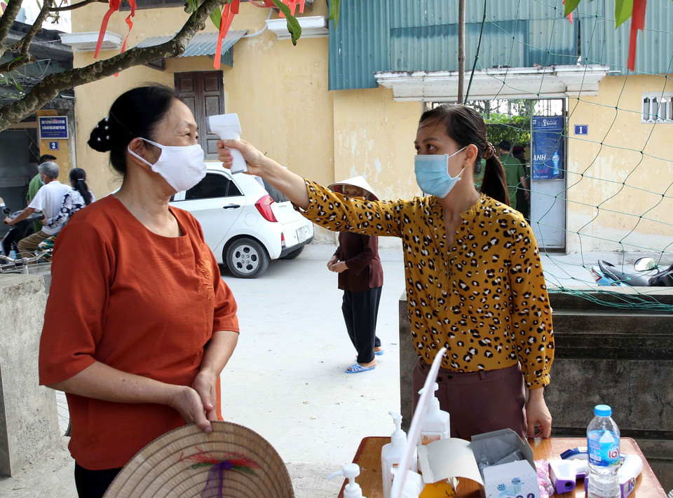 Kiểm tra thân nhiệt các cử tri để phòng, chống dịch COVID-19 trước khi vào bỏ phiếu bầu cử tại điểm bầu cử số 04, thôn Đào Xá, xã Hoàng Long, huyện Phú Xuyên, Hà Nội. (Ảnh: Phạm Kiên/TTXVN)