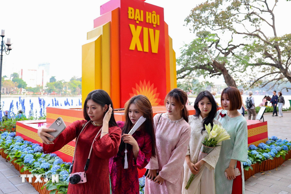 Các bạn trẻ chụp ảnh lưu niệm bên cụm trang trí chào mừng Đại hội lần thứ XIV của Đảng tại khu vực hồ Hoàn Kiếm. (Ảnh: Vũ Quang/TTXVN)