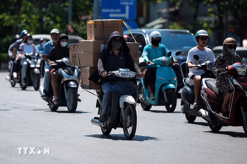 Người giao hàng bằng xe máy phải phủ kín người bằng áo chống nắng, khẩu trang và mũ để thích nghi với thời tiết khắc nghiệt. (Ảnh: Phạm Tuấn Anh/TTXVN)