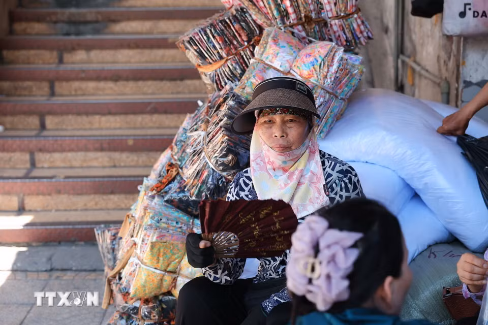Khăn che mặt, mũ rộng vành và quạt tay trở thành vật dụng quen thuộc của người bán hàng khi phải ngồi nhiều giờ ngoài trời. (Ảnh: Phạm Tuấn Anh/TTXVN)