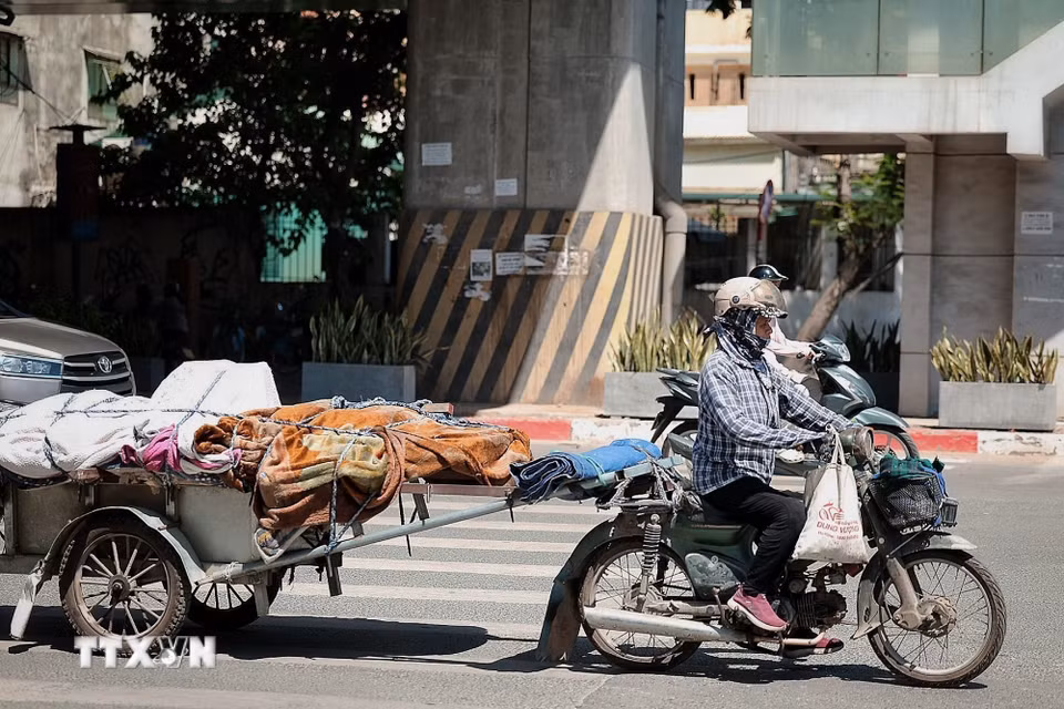Người phụ nữ che kín mặt khi chở hàng trên phố trong nắng gắt để hạn chế tác động của ánh nắng trực tiếp. (Ảnh: Phạm Tuấn Anh/TTXVN)