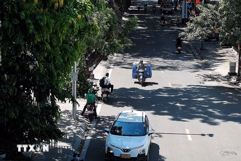 Dòng phương tiện thưa hơn vào giữa trưa; nhiều người đi xe máy cố bám sát các khoảng bóng cây để giảm bớt hơi nóng từ mặt đường. (Ảnh: Phạm Tuấn Anh/TTXVN)