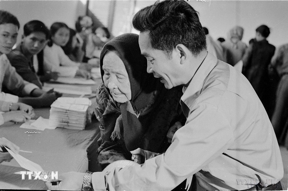 Để thể hiện tính liên tục của Nhà nước qua các giai đoạn đấu tranh cách mạng, Quốc hội đã quy định khóa Quốc hội của nước Việt Nam thống nhất là Quốc hội khóa VI. Trong ảnh: Mặc dù già yếu, Cụ Lê Thị Dưỡng (86 tuổi, đường Lý Thường Kiệt, TP.Huế), vẫn nhờ người cõng đến hòm phiếu tham gia bầu cử Quốc hội khóa VI (25/4/1976). (Ảnh: Sỹ Thái/TTXVN)