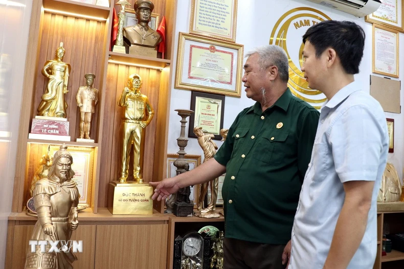 Cựu chiến binh Phan Trọng Điền (trái) giới thiệu sản phẩm đúc đồng của công ty. (Ảnh: Nguyễn Lành/TTXVN)