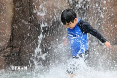 Em nhỏ làm mát dưới đài phun nước ở Incheon, Hàn Quốc ngày 13/7. (Ảnh: Yonhap/TTXVN)
