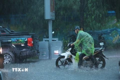 Nhiều người đi xe máy phải xuống dắt bộ vì mưa quá lớn. (Ảnh: Hoàng Hiếu/TTXVN)