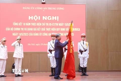 Tổng Bí thư Tô Lâm gắn huy hiệu “Anh hùng lực lượng vũ trang nhân dân” lên lá cờ truyền thống của Cục An ninh mạng và phòng, chống tội phạm sử dụng công nghệ cao, Bộ Công an. (Ảnh: Phạm Kiên/TTXVN)