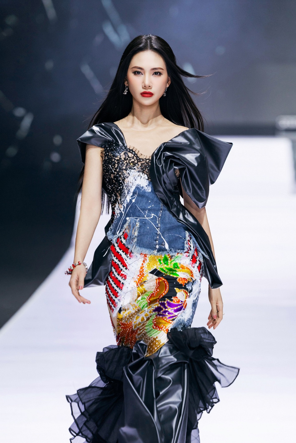 Khép lại hành trình, vedette Bùi Quỳnh Hoa – Hoa hậu Hoàn vũ Việt Nam trình diễn thiết kế dáng đuôi cá được xử lý theo hướng tái cấu trúc, kết hợp giữa denim, thổ cẩm thêu tay và các mảng đính kết thủ công tạo hiệu ứng thị giác nổi bật. Phần vai dựng phom mang tính điêu khắc, đối lập với phần tầng voan bồng nhẹ ở chân váy, tạo chuyển động mềm mại nhưng đầy kịch tính. Đây là thiết kế thể hiện rõ tay nghề và tư duy pha trộn chất liệu đặc trưng của Cao Minh Tiến. (Ảnh: CTV/Vietnam+)