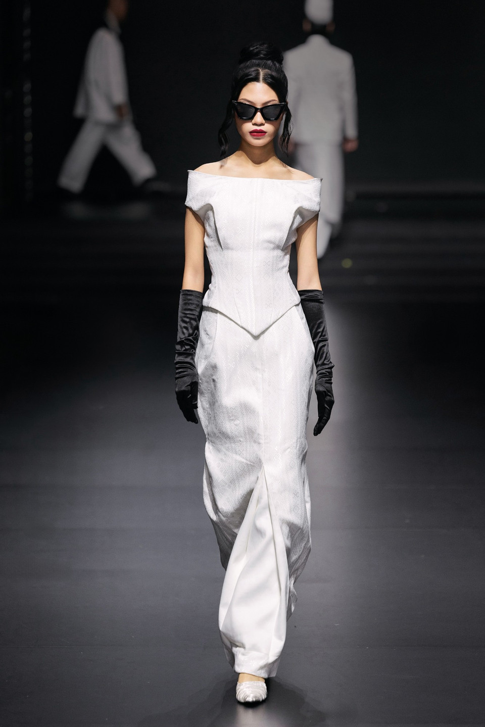 Ngược lại, các thiết kế dành cho nữ lại thể hiện vẻ thanh lịch với phom dáng cầu kỳ, được điểm xuyết bằng găng tay nhung đen mang âm hưởng cổ điển kết hợp cùng kính mát đen cá tính – tạo nét giao thoa thú vị giữa truyền thống và đương đại. (Ảnh: CTV/Vietnam+)