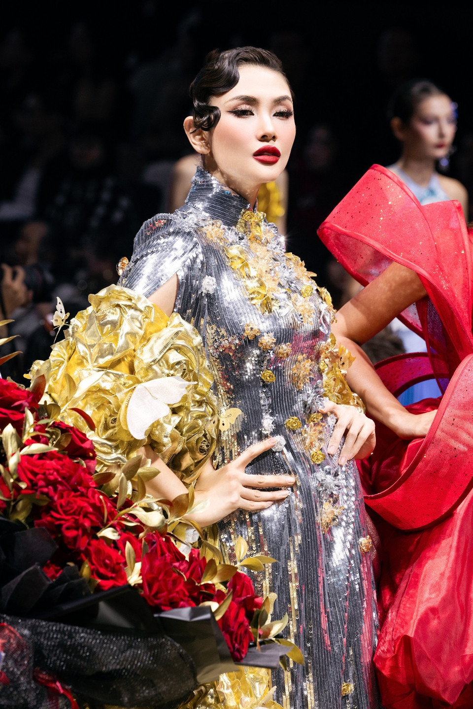 Điểm nhấn chính nằm ở phần áo choàng cape siêu dài, được phủ kín bởi hàng trăm bông hoa 3D thủ công tông vàng ánh kim, mô phỏng những cánh hoa nở rộ lúc bình minh, đúng như tên gọi “Rose of the Dawn.” (Ảnh: CTV/Vietnam+)