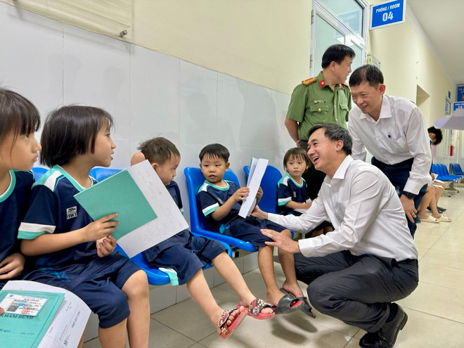 Lãnh đạo Bộ Y tế thăm hỏi trẻ em làm thủ tục chờ khám bệnh. (Ảnh: PV/Vietnam+) qua 4.jpg