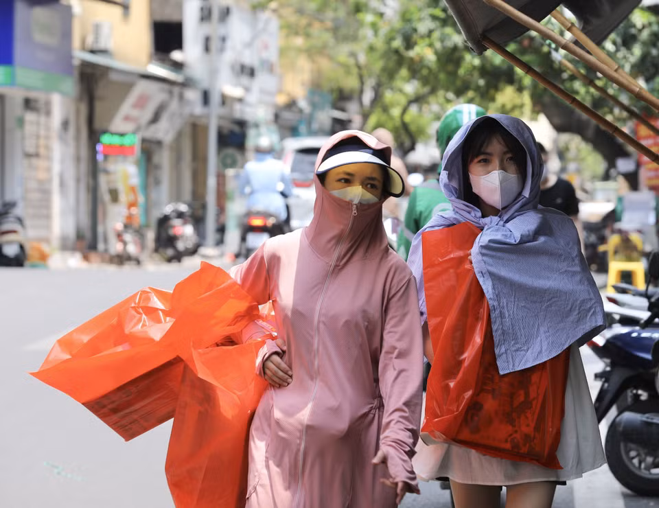 Người dân mặc đồ kín mít tránh nắng, nóng khi phải di chuyển trên đường ngày 28/6. (Ảnh: Hoàng Hiếu/TTXVN)