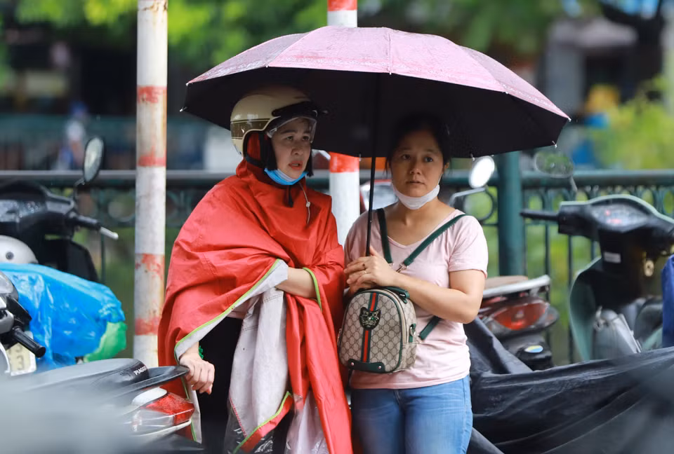 Các bậc phụ huynh 'trang bị' đầy đủ mũ áo, ô dù, sẵn sàng đồng hành cùng con bất chấp mọi điều kiện thời tiết. (Ảnh: PV/Vietnam+)