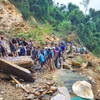 Người dân dùng xà beng, búa tạ phá nhỏ những tảng đá lớn tại điểm sạt lở trước khi kích nâng lên thanh trượt để dịch chuyển sang mép vực, tạo lối mở qua điểm sạt lở. (Ảnh: TTXVN phát)