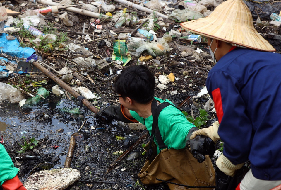 Lượng rác rất dày khiến các thành viên phải dùng cào để kéo rác từ dưới dòng sông. (Ảnh: Tuấn Anh/TTXVN)