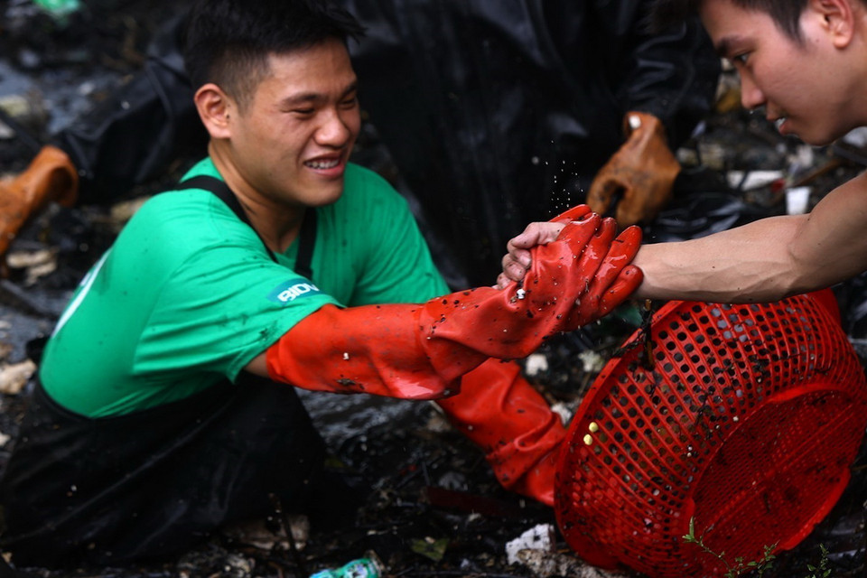 Các thành viên hỗ trợ nhau tìm chỗ đứng để vớt rác ở những vị trí khó khăn dưới dòng sông. (Ảnh: Tuấn Anh/TTXVN)