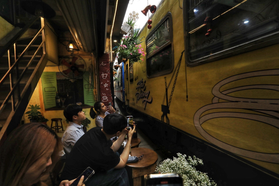 Du khách ngồi uống càphê ngay sát đường tàu khi tàu chạy qua. (Ảnh: Tuấn Anh/TTXVN)