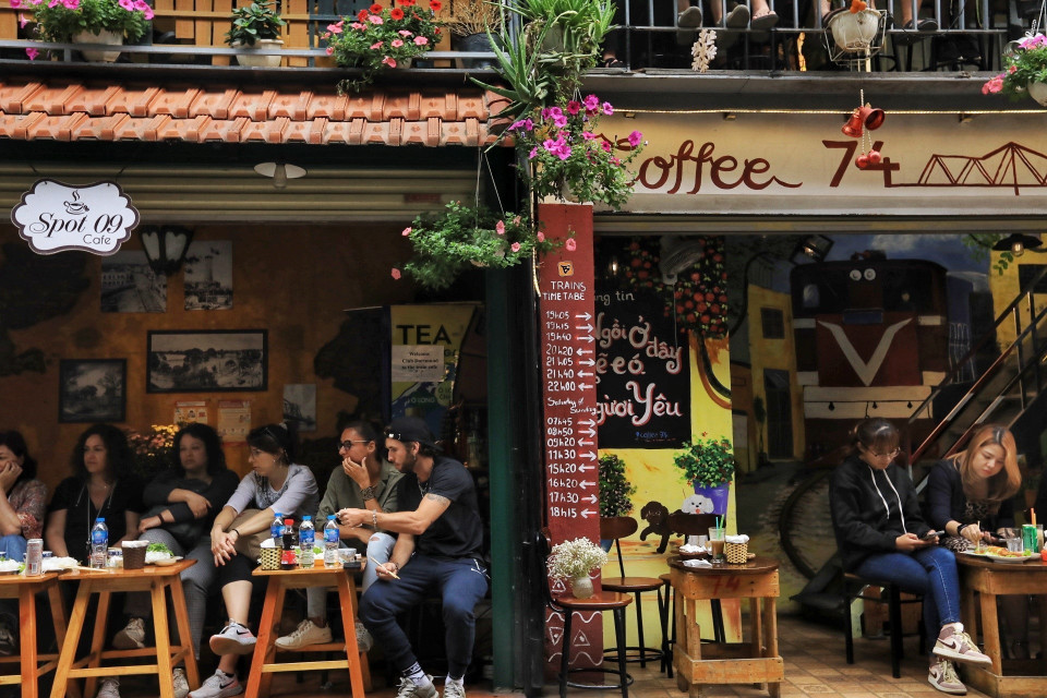 Du khách nước ngoài chủ động tụ tập tại các quán "cà phê đường tàu," chờ đến giờ tàu chạy qua để trải nghệm bởi khung giờ tàu chạy được dán trước cửa quán càphê (ảnh chụp chiều 4/3). (Ảnh: Tuấn Anh/TTXVN)