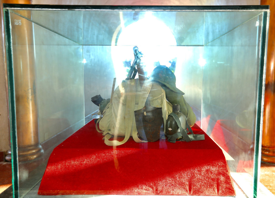 Chính giữa Đài tưởng niệm là nơi đặt hành trang người lính: Một chiếc mũ tai bèo, đôi dép cao su, một bi đông nước, khẩu súng AK và chiếc balô, giản dị và thân thương mà các anh đã làm nên lịch sử. (Ảnh: Hoàng Hiếu/TTXVN)