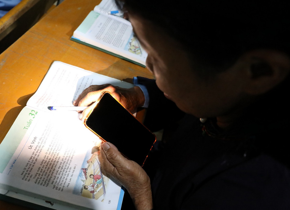 Nhiều học viên cao tuổi vẫn miệt mài đến lớp soi đèn pin điện thoại đọc từng con chữ mỗi khi đêm về. (Ảnh: Văn Đạt/TTXVN)