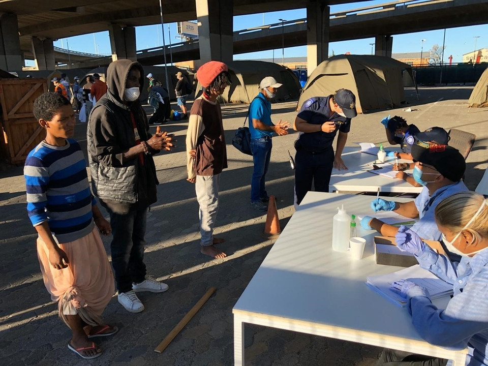 Để ngăn đà lây lan của dịch COVID-19, Chính phủ Nam Phi tiến hành nhiều biện pháp giúp người vô gia cư có được mái nhà tạm cùng những bữa ăn miễn phí trong 21 ngày nước này áp dụng lệnh phong tỏa trên quy mô toàn quốc. Lực lượng chức năng ghi chép thông tin cá nhân của người vô gia cư trước khi cho họ vào khu nhà tạm. (Ảnh: Phi Hùng/TTXVN)