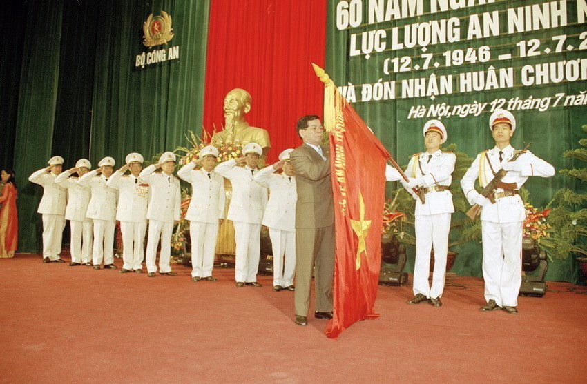 Chủ tịch nước Nguyễn Minh Triết gắn Huân chương Sao Vàng lên lá cờ truyền thống của của Tổng cục An ninh, Bộ Công an tại Lễ kỷ niệm 60 năm Ngày truyền thống lực lượng An ninh nhân dân (12/7/2006). (Ảnh: Tùng Lâm/TTXVN)