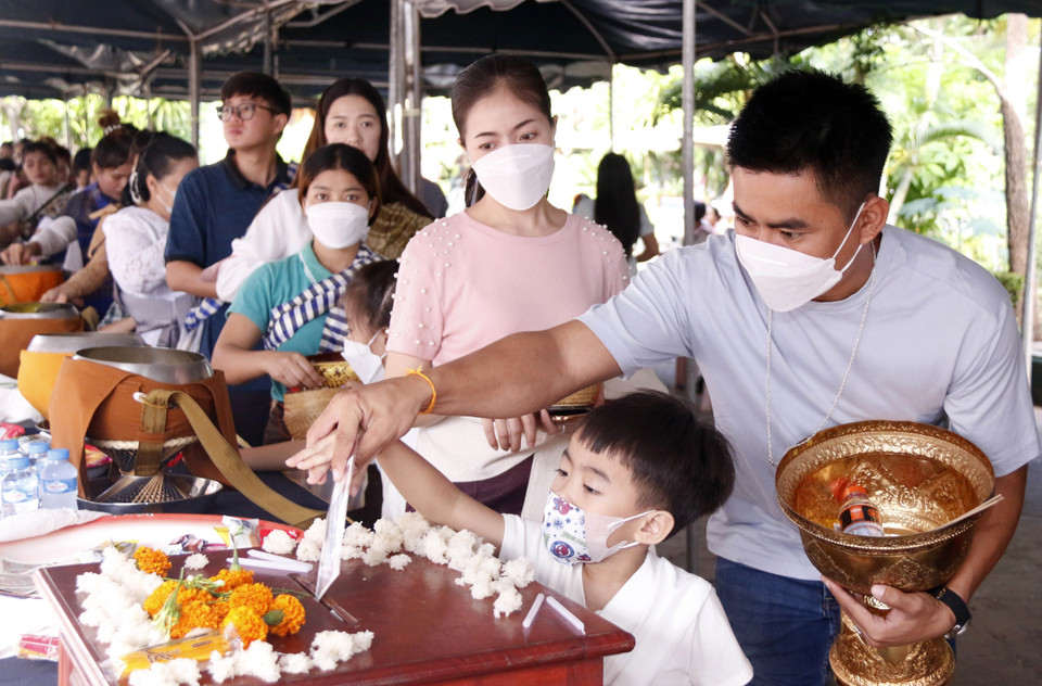 Một người cha hỗ trợ con thực hiện nghi thức Tatbath, một trong các nghi lễ trong Boun Okphansa. (Ảnh: Phạm Kiên/TTXVN)