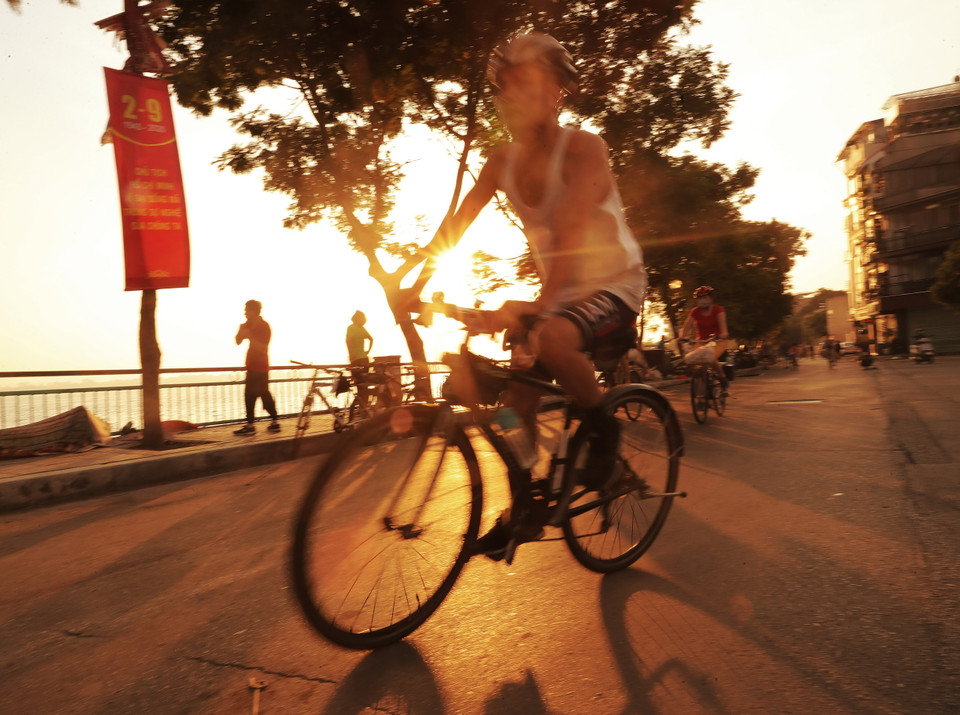 Người dân đạp xe trong nắng sớm bên Hồ Tây. (Ảnh: Lâm Khánh/TTXVN)