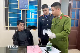 Đối tượng Trần Văn Dương (ngồi) cùng tang vật bị lực lượng chức năng thu giữ. (Ảnh: TTXVN phát)