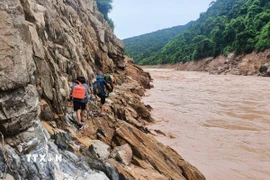 Tổ công tác di chuyển theo vách đá ngược thượng nguồn sông Nậm Mộ trên hành trình tiếp cận bản Cha Nga - một trong nhiều bản làng ở Nghệ An bị cô lập do nước lũ và tình trạng sạt lở trong vài ngày qua. (Ảnh: TTXVN phát)