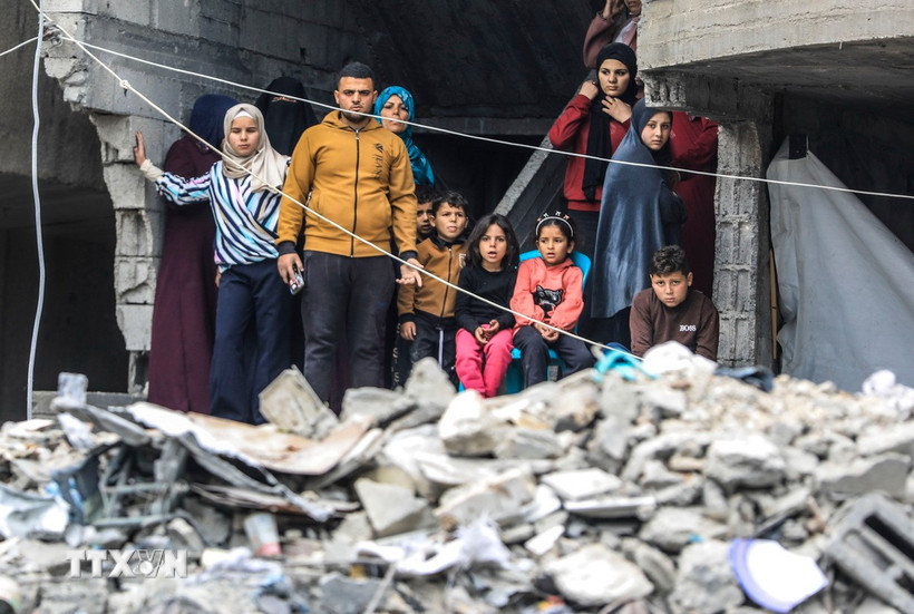 Người dân Palestine đứng trên đống đổ nát của những tòa nhà bị phá hủy sau các cuộc không kích của Israel xuống Dải Gaza. (Ảnh: THX/TTXVN)