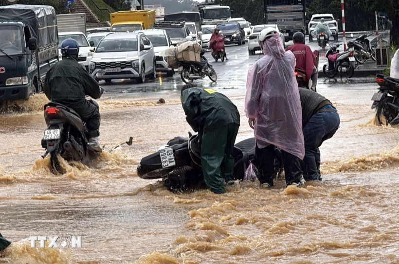 Lực lượng dân quân hỗ trợ một người điều khiển xe máy bị ngã khi đi qua đoạn đường ngập nước trước cổng Vườn hoa thành phố Đà Lạt. (Ảnh: Nguyễn Dũng/TTXVN)