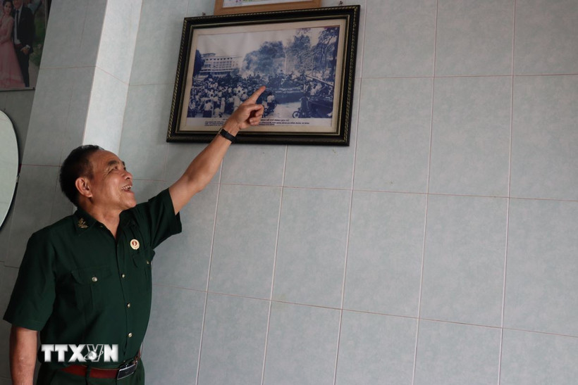 Cựu chiến binh Trần Dân bên bức hình chụp cùng đồng đội tại Dinh Độc Lập vào 13h30 ngày 30/4/1975. (Ảnh: Hoàng Ngà/TTXVN)
