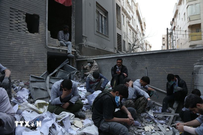 Người dân ngồi trên đống đổ nát của những tòa nhà bị phá hủy do xung đột tại Tehran, Iran ngày 15/3/2026. (Ảnh: THX/TTXVN)