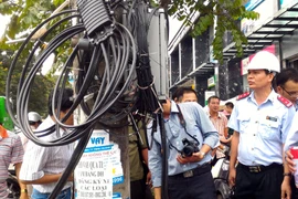 Chánh thanh tra Nguyễn Văn Minh (đội mũ) kiểm tra việc chấp hành quy định về cáp viễn thông tại phố Thái Hà. (Ảnh: T.H/Vietnam+)