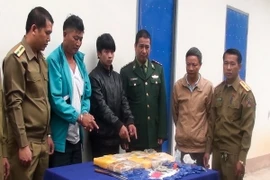 Hai đối tượng (áo khoác xanh và áo đen) cùng tang vật tại cơ quan điều tra. (Ảnh: TTXVN phát)