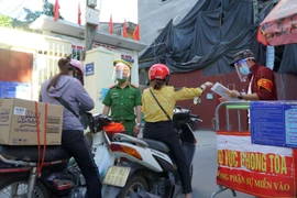 Thành viên Tổ COVID-19 cộng đồng đang cùng lực lượng công an kiểm tra người dân ra vào khu vực chốt phong tỏa. (Ảnh: Minh Hiếu/Vietnam+)