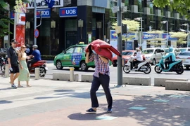 Một người dân tại Thành phố Hồ Chí Minh dùng áo che kín đầu, bước vội giữa trời nắng nóng. (Ảnh: Hồng Giang/TTXVN)