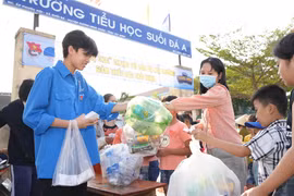 Đoàn viên Thanh niên xã Suối Đá thu gom chai nhựa sử dụng một lần và phát phiếu tham gia phiên chợ chai cho người dân. (Ảnh: Minh Phú/TTXVN)